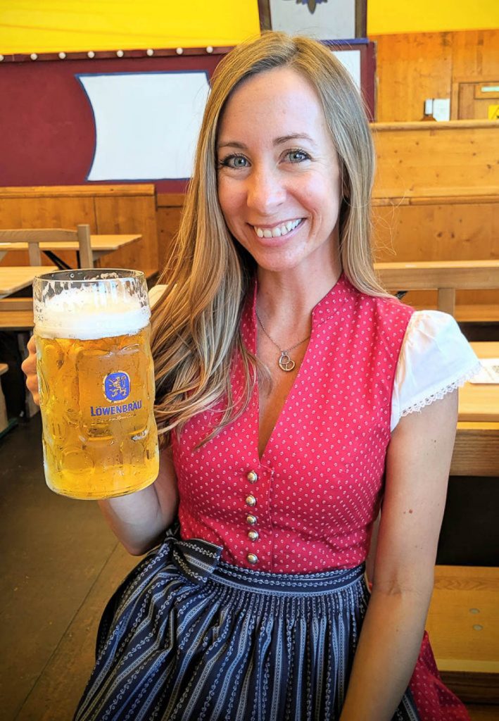 me in a red and blue dirndl holding up a beer inside a beer tent in munich at oktoberfest