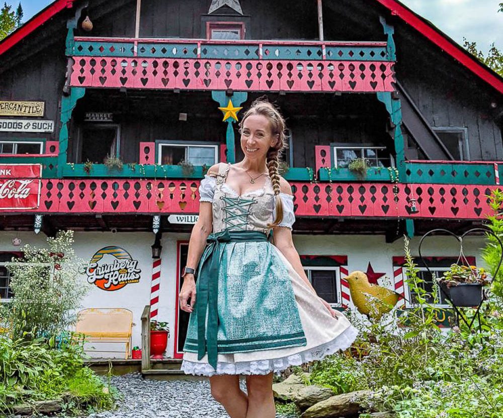 me in a teal and beige dirndl in front of an alpine cottage in vermont