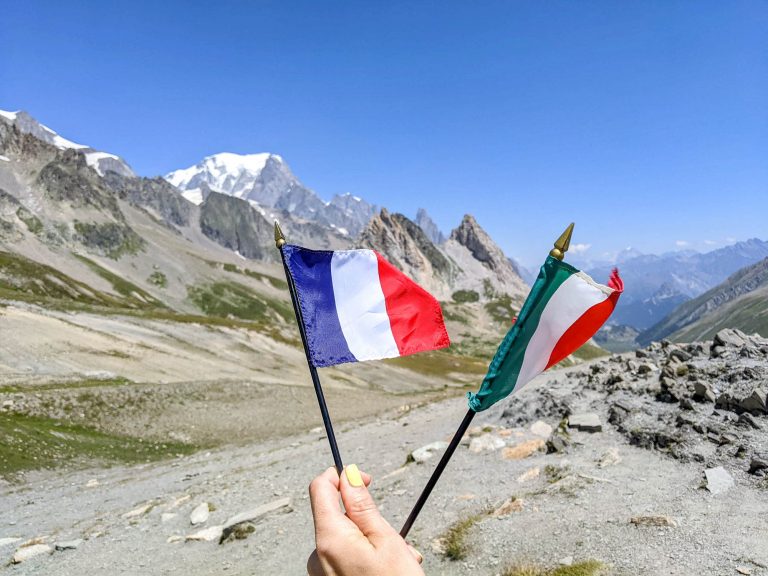 hand hold and a france and italy flag in front of some mountains