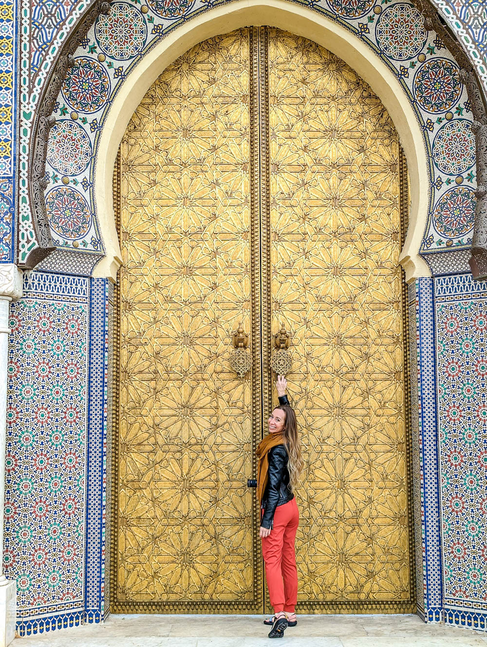small girl in red pants in front of a giant gold door