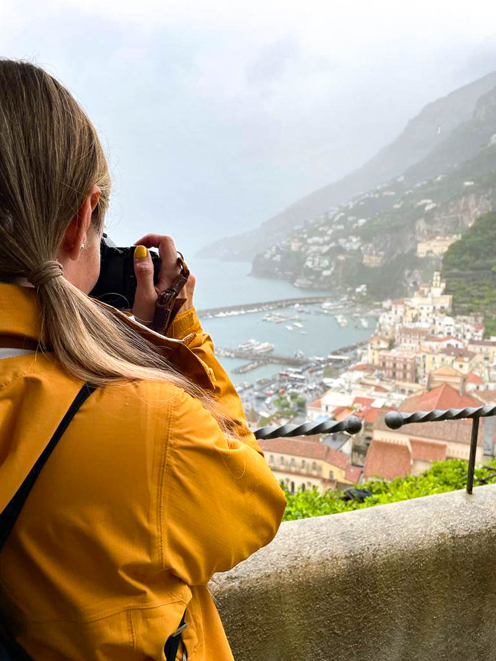 woman in yellow jacket taking a photo of a city from a lookout point