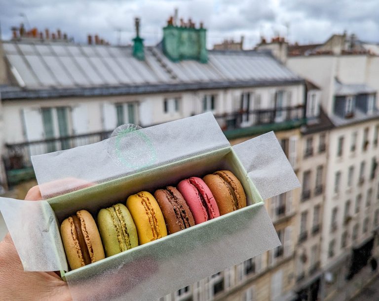 hand holding box of colorful macarons in front of a Paris skyline