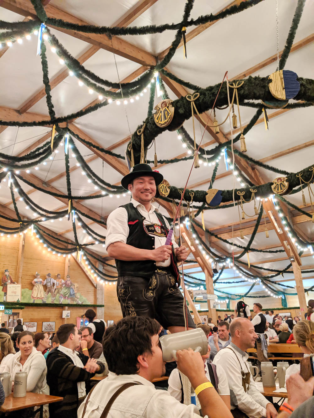 man standing on a table in an oktoberfest beer tent holding a whip