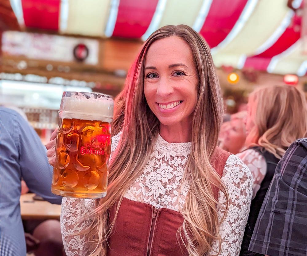 woman in lace shirt holding a large beer under a red and white striped tent