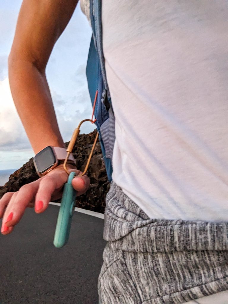 woman holding a small blue piece of equipment that's tied to her bag